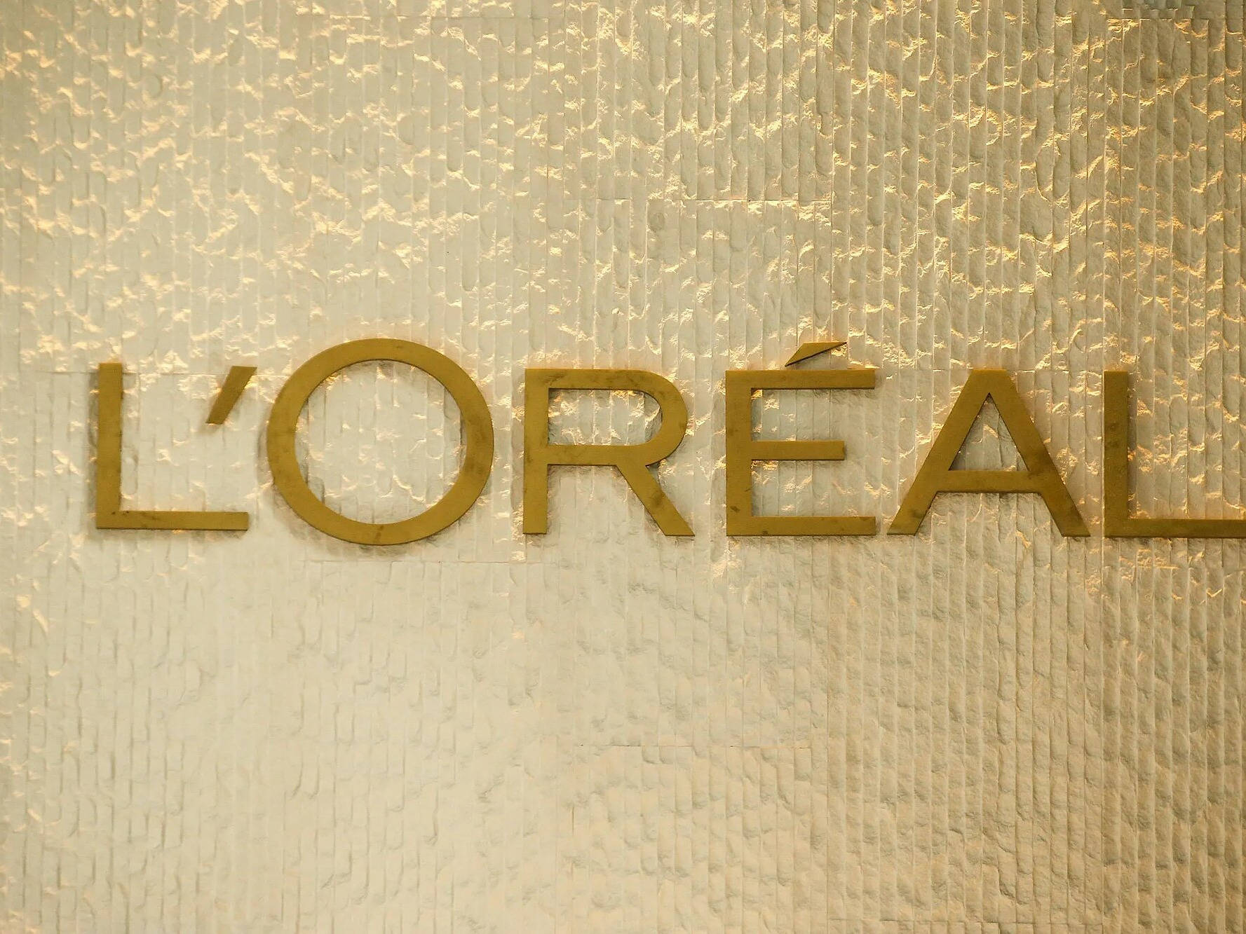 The L’Oréal wordmark in gold on a textured wall